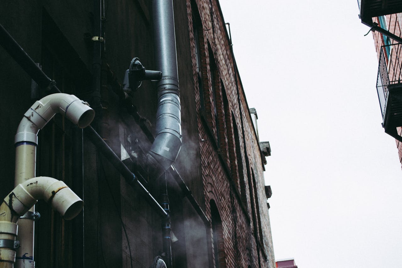 A moody urban alley displaying exposed metal pipes and smoke, showcasing industrial architecture.