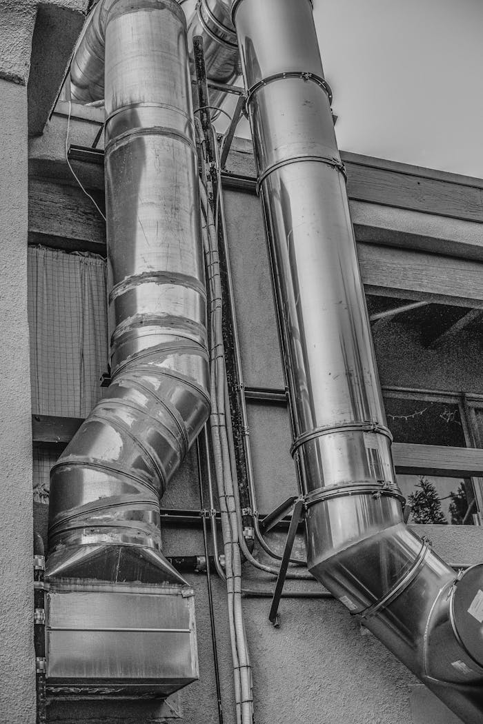 Black and white image showcasing large steel pipes on a building exterior.