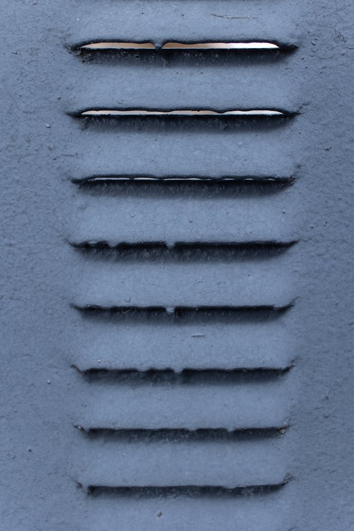 Close-up photo of a metal ventilation grate with textured surface and visible light reflections.